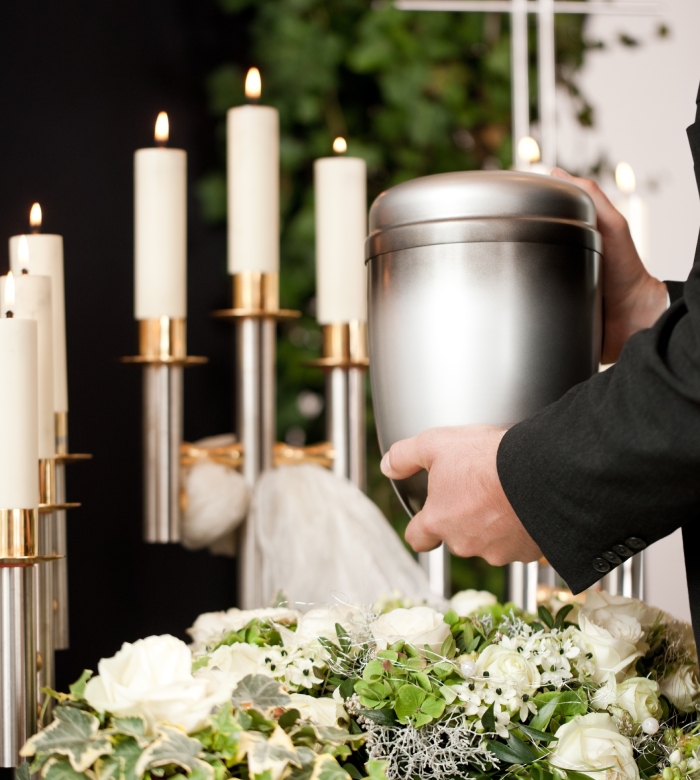 Urne funéraire en métal entourée de fleurs blanches et de bougies lors d’une cérémonie d’obsèques